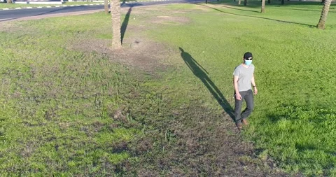 Young man in black cap and protective mask walking through a park. Stock Footage 135226809