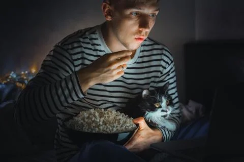 Young man with black cat watching a movie eating popcorn on TV at home. Movie Stock Photos