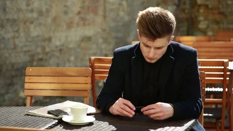 Young Man in a black Coat sitting alone at the Table Cafe 스톡 동영상 80601954