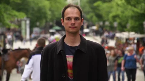 A young man in a black coat stands among walking people Stock Footage 337427446
