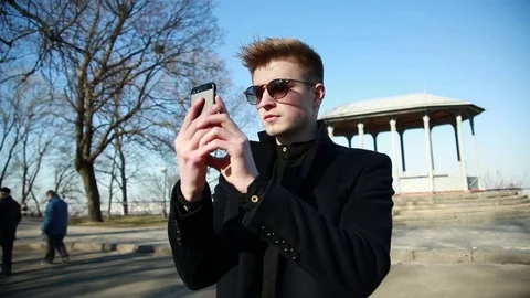 Young Man in Black Coat take Photo with Mobile Smart Phone in Spring Park Stock Footage 80602260