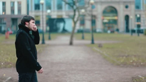 A young man in a black coat is talking on the phone in the autumn park. Stock Footage 131520106