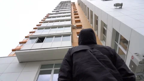Young man in a black hooded jacket looks at an apartment building Stock Footage 153966175