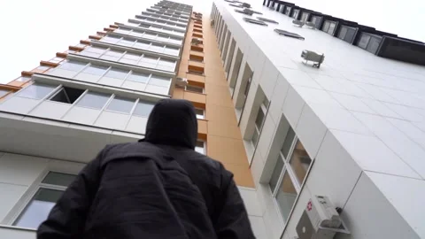 Young man in a black hooded jacket looks at an apartment building Stock Footage 167930868