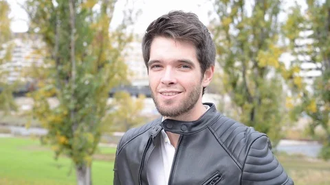 Young man with black jacket and white shirt looks and smiles at camera. Видео 120740617