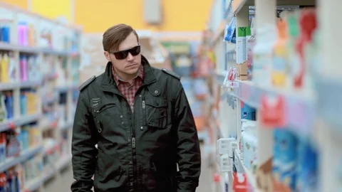 A young man in a black jacket and sunglasses steals in a store Stock Footage 126833069