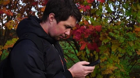 Young man in black jacket in the autumn park using his smartphone Stock Footage 69945940