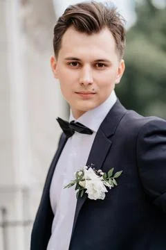Young man in a black jacket with a bud of flowers stands on street near building Stock Photos