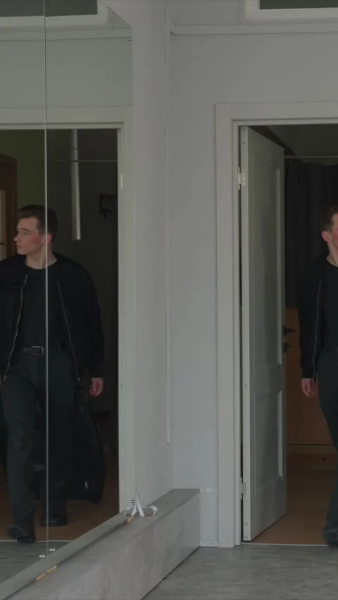 Young Man in Black Jacket Exits Through Open Door with Rolling Suitcase in Stock Footage 343083462