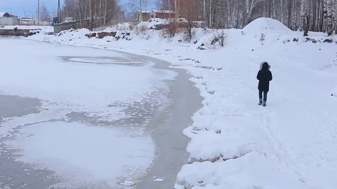 Young man in black jacket with fur hood is on snow-covered Bank of frozen river Stock-Footage 99420873