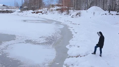 Young man in black jacket with fur hood is on snow-covered Bank of frozen river Video stock 99420898