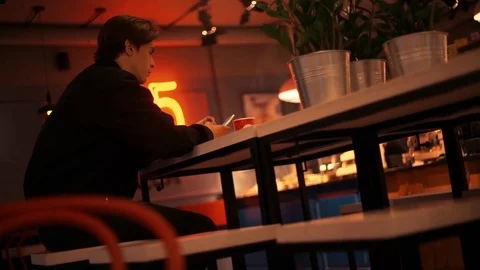 Young man In black jacket typing messages on smartphone in cafe in the evening Stock Footage 77168599