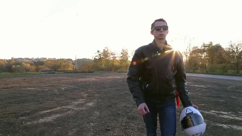 A young man in black leather jacket with white helmet sits on motorcycle Video stock 81492642