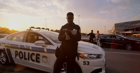 Young man black policeman leaning on car hood writing a fine doing his job under Stock-Footage 112953709
