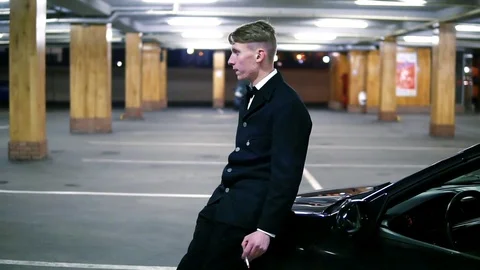 Young man in a black suit with a bow-tie smoking a cigarette sitting at the Видео 72954236