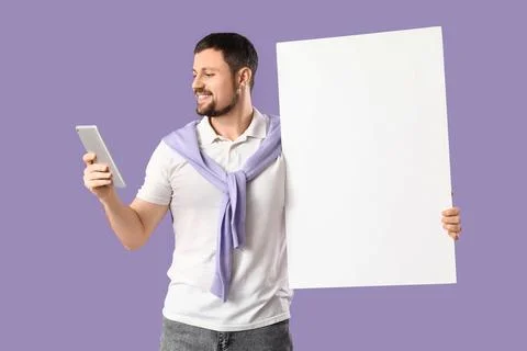 Young man with blank poster using tablet computer on lilac background Stock Photos