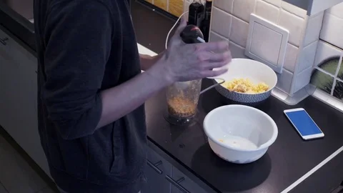Young man with blender preparing vegetable food and watching video at smartphone Stock Footage 74158856