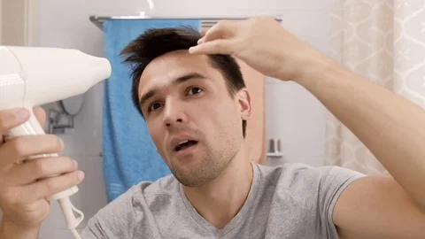 Young man blow drying his hair in a bathroom. Stock Footage 115188182