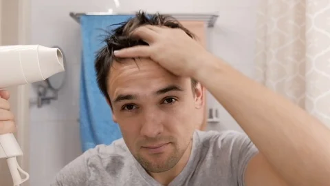 Young man blow drying his hair in a bathroom. Stock Footage 115188365