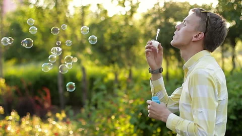 Young man blowing soap bubbles in the garden Stock Footage 90399538
