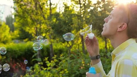 Young man blowing soap bubbles in the garden Stock-Footage 93389825