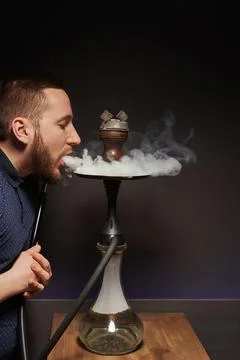 A young man blows a cloud of white smoke on a hookah saucer Stock Photos