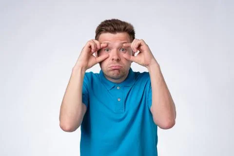 Young man in blue clothes trying to open eyes with fingers, sleepy and tired Stock Photos