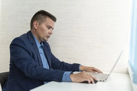 A young man in a blue jacket is working on a laptop at home in quarantine. Bu Stock Photos