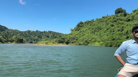Young Man in Boat, Camera Pans to Tropical River Landscape, Wide Shot Stock Footage 324772617