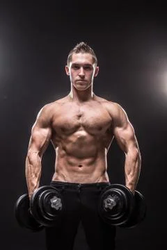 Young man bodybuilder looking at camera holding dumbbells Stock Photos