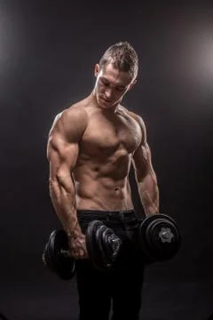 Young man bodybuilder looking down holding dumbbells, side view. Stock Photos