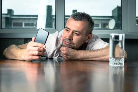 Young man bored using his smartphone. Bored young man sitting in his kitchen  Stock Photos