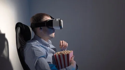 A young man with a box of popcorn in his hand watching a video in a virtual Stock Footage 101847944