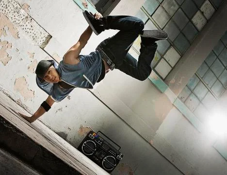 A young man breakdancing on the street of a city, doing a one handed handstand. Stock Photos