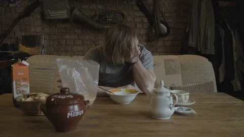Young man at the breakfast table eating cereal and pours tea Stock Footage 81295428