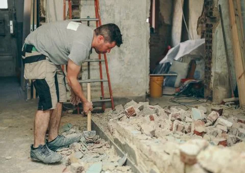 A young man breaks a brick wall with a sledgehammer. Stock Photos