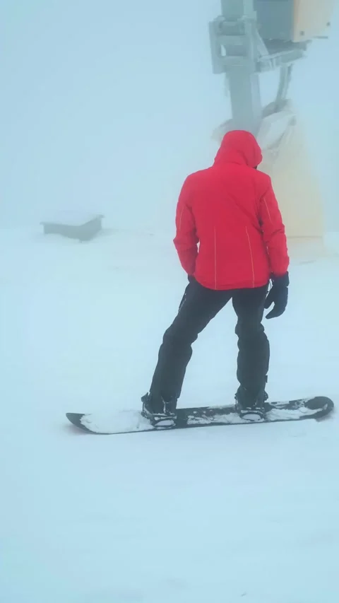 Young man in a bright red jacket snowboards down a mountain slope, showcasing th Video stock 280186525