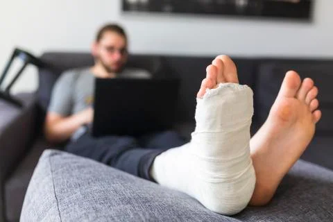 Young man with a broken leg on the sofa Stock Photos