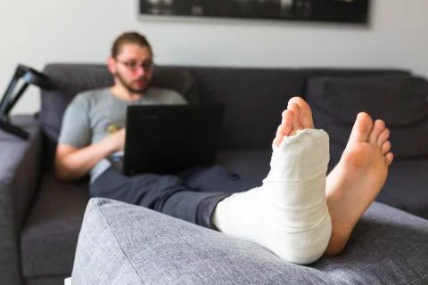 Young man with a broken leg on the sofa Stock Photos