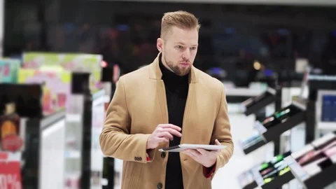 Young man in brown coat use digital tablet walk in shopping mall, steadicam shot Stock Footage 121188276