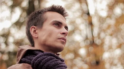 Young man in brown jacket and knitted scarf in autumn park drinks coffee out of Stock Footage 68351266