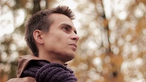 Young man in brown jacket and knitted scarf in autumn park drinks coffee out of Video stock 68352811