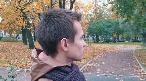 Young man in brown jacket and knitted scarf in autumn park drinks coffee out of Stock Footage 68365663