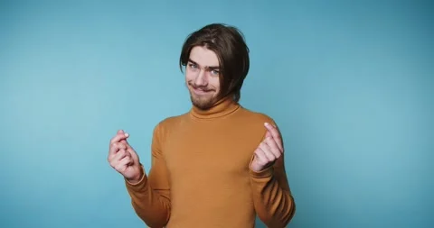 Young man in a brown turtleneck gesturing heart with fingers against blue b.. Stock Footage 315162925