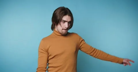 Young man in a brown turtleneck is playfully pointing away, suggesting move.. Stock Footage 313280468