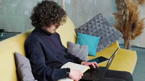 Young man is browsing at his laptop and writing notice on his paper notebook. Stock Footage 152978769