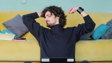 Young man is browsing at his laptop and stretches up his hands, working at the Stock Footage 153480431