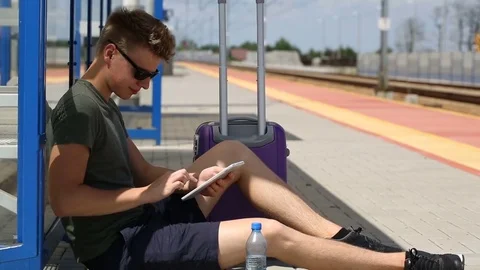 Young man browsing internet on tablet while waiting for his train on the station Stock Footage 78654195