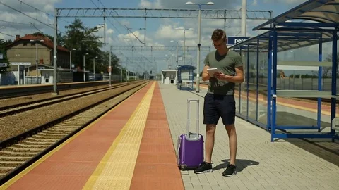Young man browsing internet on tablet while waiting for the train Stock Footage 78656198