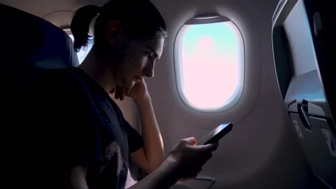 Young man browsing mobile phone during airplane journey by window seat 库存影片 334041064